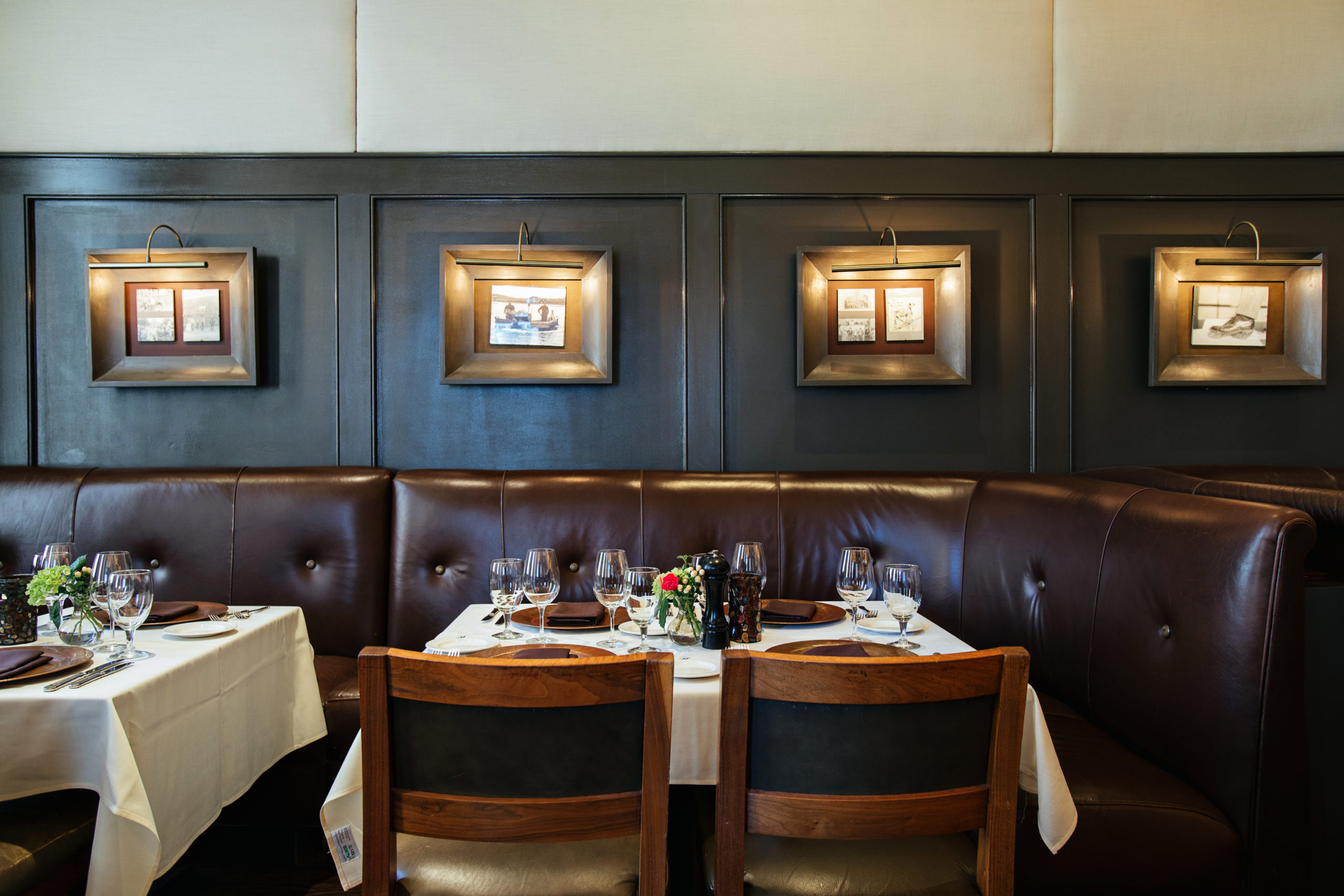 Elegant dinner table with table linens, leather booth seating and a feature wall of artwork lit by overhead lamps