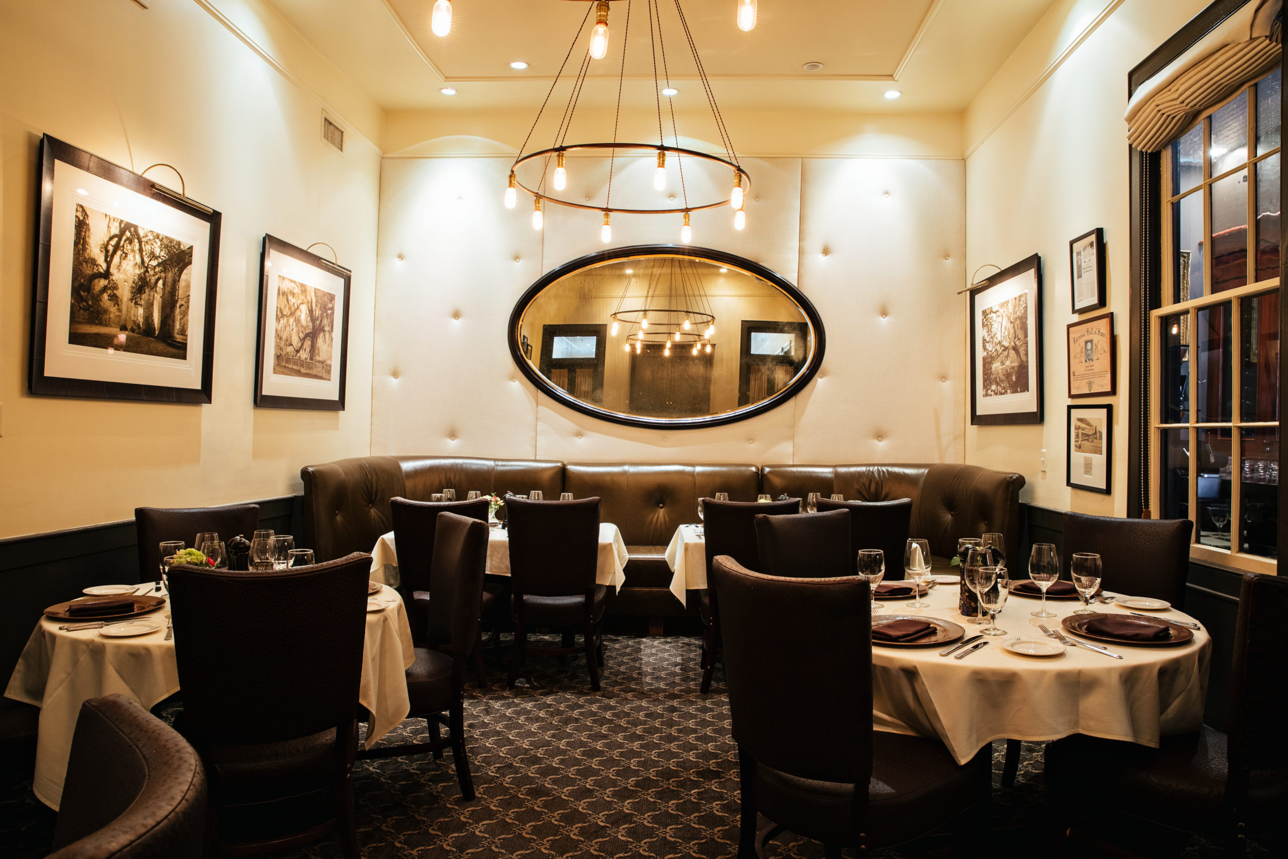 Cozy restaurant dining room with oval mirror on the back wall, accent artwork and large round chandelier overhead