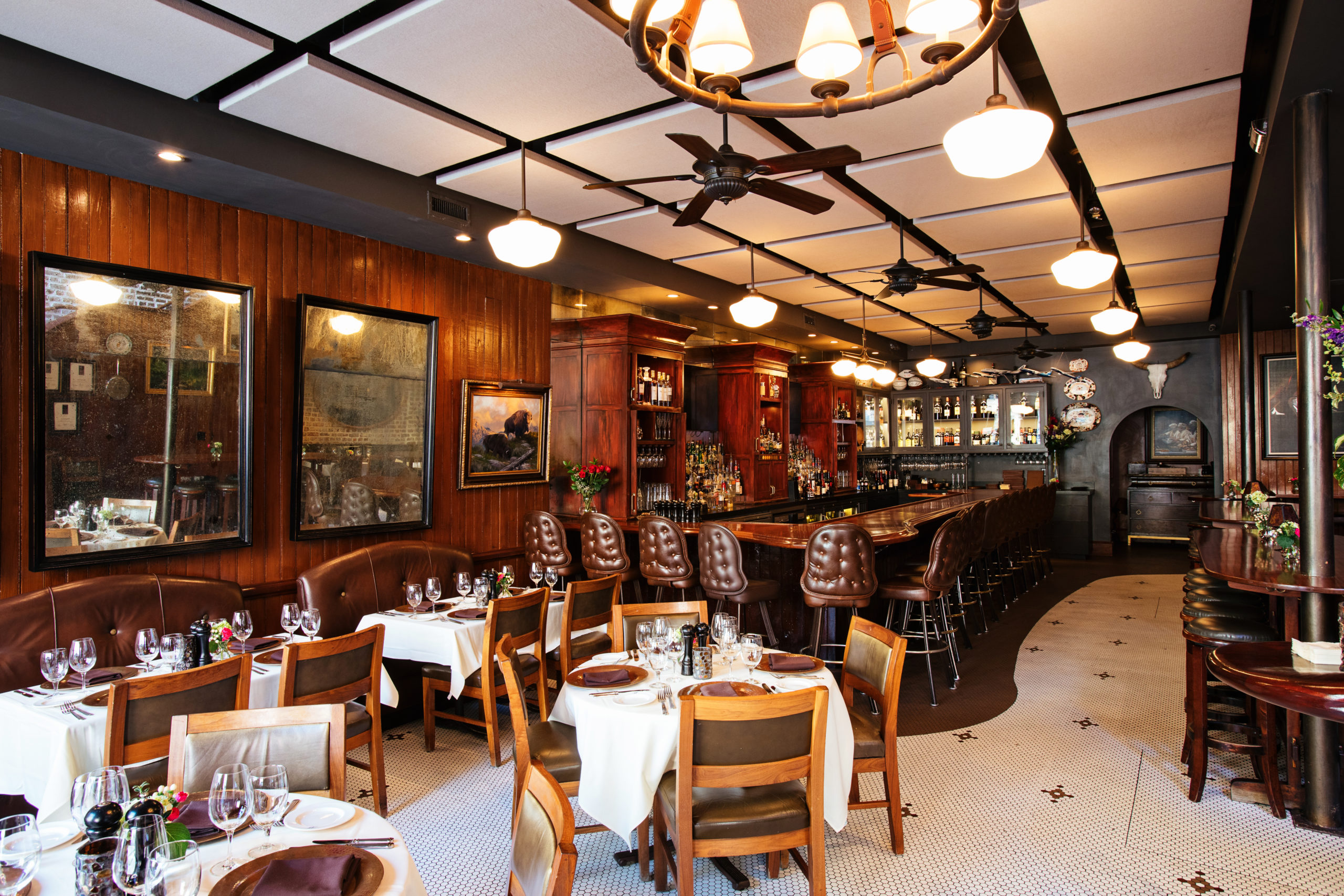 restaurant bar with leather bar stools, dark wood paneling, and intimate dining tables with elegant table settings