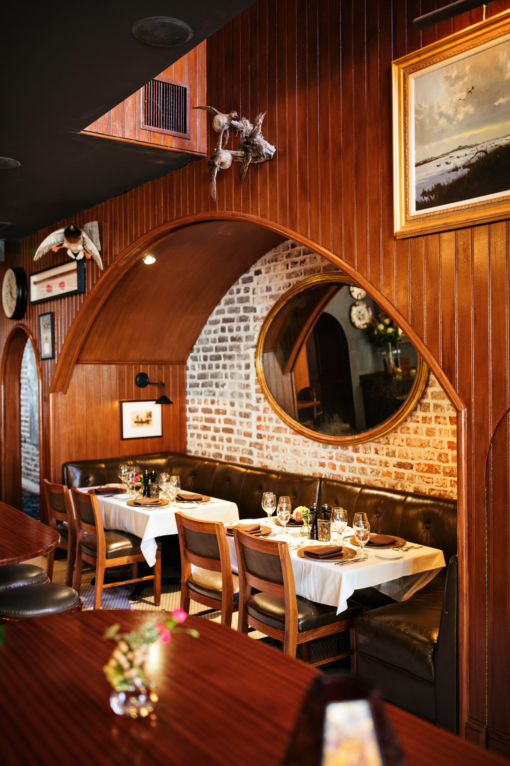 Oval mirror inside a wood arched wall with dining tables underneath