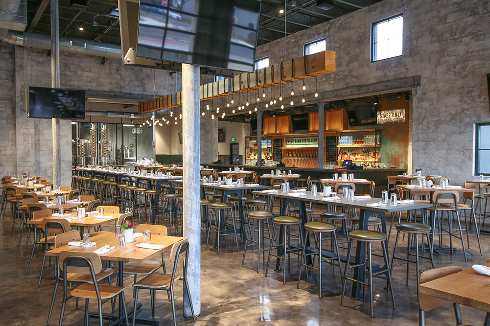 large back lite bar with a row of high top tables and barstools in front and a row of square tables of four