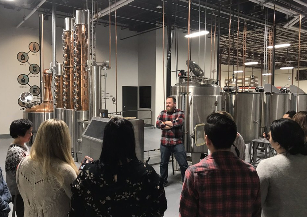 A group of people receiving a tour of the distillery in front of the distillery machinery