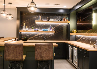 basement bar with globe lights, leather barstools and wood floating shelves