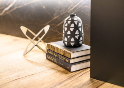 black and white vase on top of three books and a gold metal sculpture on a wood shelf
