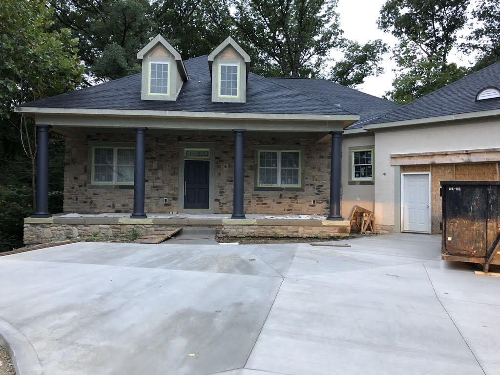 Construction of a home with roof, stone, columns and windows but siding is not complete