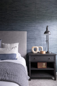 Stunning blue master/primary bedroom with wallpaper, beautifully decorated bed with throw pillows. Nightstand with industrial lamp